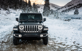 SUV Jeep Wrangler Unlimited Sahara, 2018 on a snow-covered road against the backdrop of the mountains