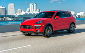 Красный автомобиль Porsche Cayenne на фоне города 