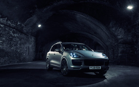 Серебристый автомобиль Porsche Cayenne в тоннеле с включенными фарами