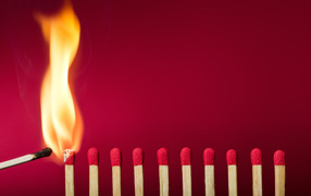 Зажженная спичка и спички на красном фоне