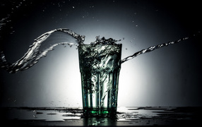 Брызги воды из стакана с водой на сером фоне