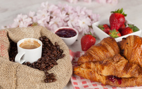 A cup of coffee in a bag with coffee beans and fresh croissants