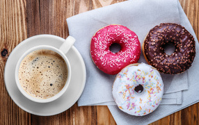 A cup of coffee with three appetizing donuts on a table