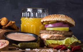 Аппетитный гамбургер на столе с соусом, овощами и соком