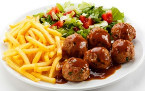 Картофель фри на белой тарелке с салатом и фрикадельками