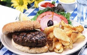 Гамбургер с котлетой и картофельные чипсы на тарелке с овощами