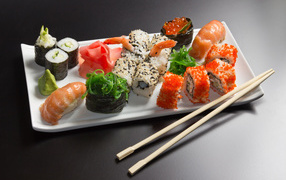 Суши и роллы на белой тарелке с палочками на сером фоне