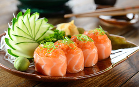 Суши из красной рыбы на тарелке со свежими огурцами и зеленью