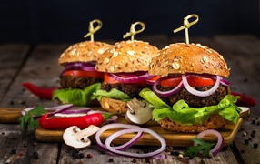 Три аппетитных гамбургера с кольцами лука и перцем