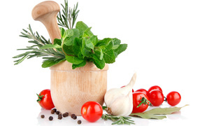 Деревянная ступа и пестик со специями и зеленью на столе с чесноком и помидорами