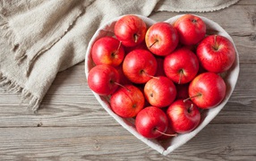 Beautiful red apples in a plate in the shape of a heart on a table