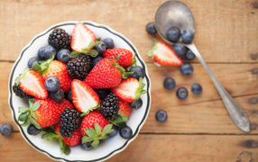 Свежие ягоды клубники, черники и ежевики в тарелке на деревянном столе
