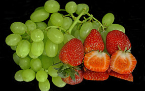 Green grapes and ripe strawberries on a black background