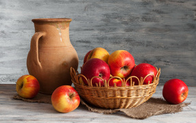 Red apples in a basket on a table with a jug