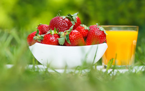 Спелые ягоды клубники и стакан апельсинового сока на зеленой траве
