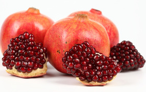 Three red pomegranates with slices on a white background