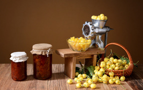 Two jars of jam and yellow cherries on a table with a meat grinder