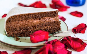 A piece of cake with chocolate cream and red rose petals