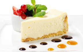 A piece of cheesecake on a white plate with berries and mint