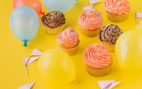 Аппетитные капкейки с кремом и воздушными шариками на желтой поверхности