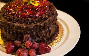 Торт с шоколадным кремом, виноградом и клубникой на белой тарелке