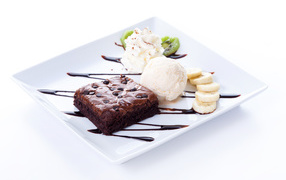 Chocolate cake with ice cream, cream and banana slices on a white plate