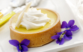 Десерт с кремом и фиолетовыми цветами на белой тарелке