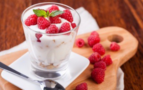 Десерт с йогуртом и свежей малиной в стеклянном стакане на столе