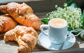 Fresh croissants with a cup of coffee and a bouquet of lilies of the valley on the table