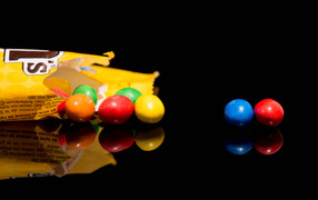 Разноцветные конфеты  M&m's отражаются в черной поверхности стола 