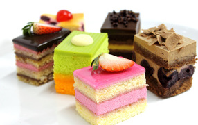 Разноцветные пирожные с ягодами на белом фоне