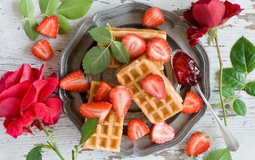 Сладкие вафли со свежей клубникой и красными розами на столе