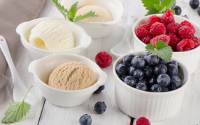 Three balls of ice cream and fresh berries of raspberries and blueberries in white plates