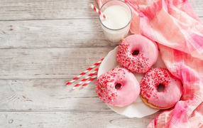 Three mouth-watering donuts with a pink sugar frosting and a glass of milk