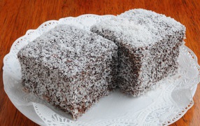 Two pieces of cake in coconut chips on a white plate