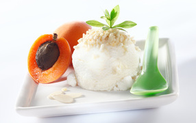 Шарик ванильного мороженого с абрикосами на белой тарелке с ложкой