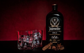 Бутылка ликера Jägermeister на столе с корицей и стаканами