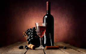 Бутылка красного вина на столе с бокалом и синим виноградом