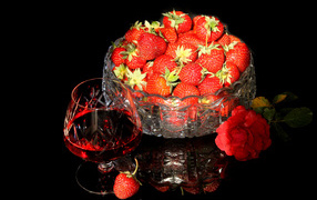 Бокал клубничного ликера на столе со спелой клубникой и красной розой