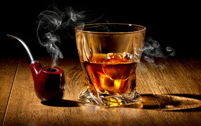 Стакан виски со льдом на столе с дымящейся трубкой