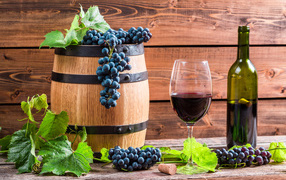 Бокал вина с бочкой и бутылкой на столе с гроздьями синего винограда с листьями