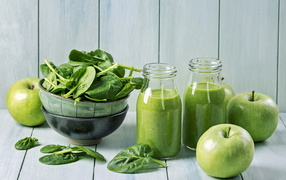 Яблочный сок в стеклянных бутылках,  свежие зеленые яблоки и зелень на столе