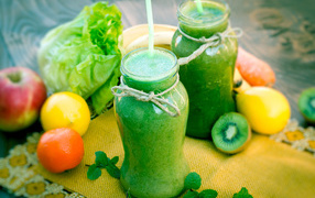 Зеленый смузи в бутылках с трубочками и фруктами на столе