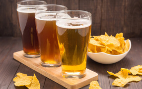 Три стакана пива на столе с чипсами