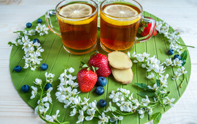 Две чашки чая с лимоном на столе с ягодами клубники, черники и кусочками имбиря