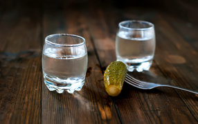 Две рюмки водки и соленый огурец на столе