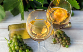 Два бокала белого вина с белым виноградом на столе