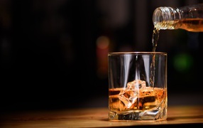 Виски наливают из бутылки в стакан со льдом