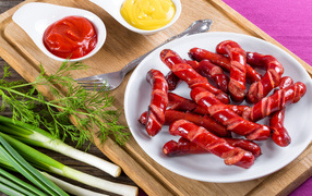 Аппетитные сосиски барбекю на столе с соусом и зеленью