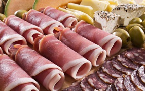 Appetizing rolls of bacon on a plate with green olives